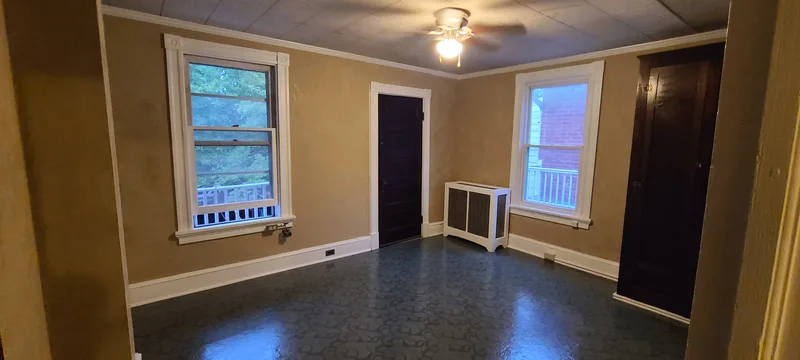 Back bedroom: taupe plaster walls, white trim, dark wood, green vinyl floor, two windows and a door onto the back porch. 