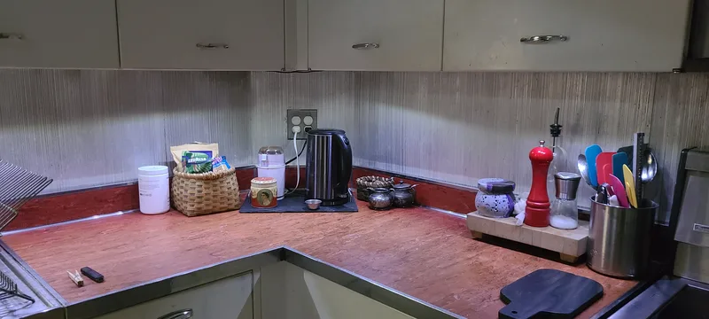 Red countertop, aluminum backsplash, cooking utensils, and coffee-making supplies lit by LED under-cabinet lights