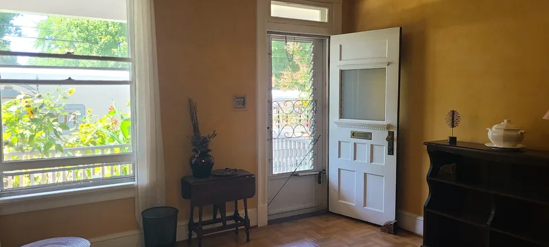White trimmed front door and window. Yellow plaster walls, parquet vinyl flooring, dark wood furniture. 