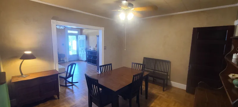 Wider angle view of the dining room, and view into living room. White trim, dark furniture, ceiling fan, parquet floors