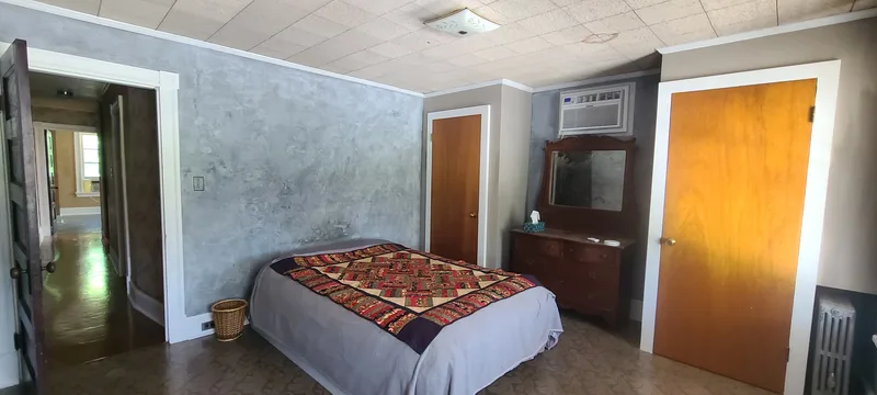 Front bedroom. Grey walls, white trim, two closets with wooden doors. Air mattress with multi-colored quilt