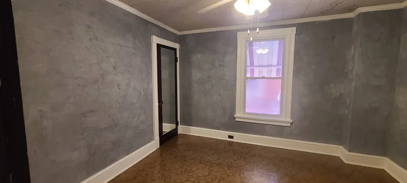 Middle bedroom, grey plaster walls, white trim, green vinyl floor, closet with mirror door