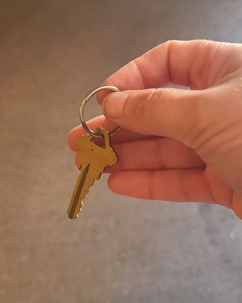 Hand holding house key on grey background