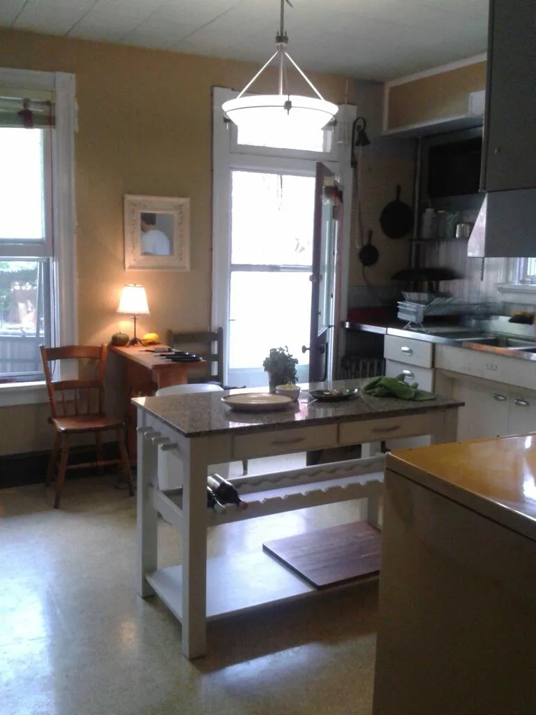View of kitchen towards back door. Island in the center of the room, window on back wall, cabinets and sink to the right